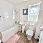 Modern bathroom with white fixtures and wood flooring.