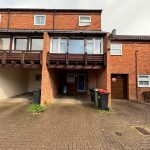 Brick terraced house with driveway and bins outside.