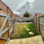 Small fenced garden with paved path and lawn.