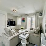 Modern living room with neutral decor and large TV.