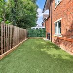 Small garden with artificial grass alongside brick house