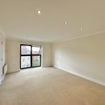 Spacious empty room with large window and beige carpet.