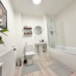 Modern bathroom with plant, shower, and shelf.