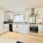 Modern white kitchen with appliances and wooden flooring.