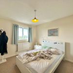 Bright bedroom with unmade bed and coats on rack.