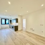 Modern empty kitchen with wooden floor and white walls.