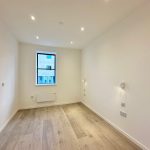 Minimalist empty room with wood flooring, single window.