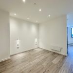 Modern empty room with wooden flooring and lights.