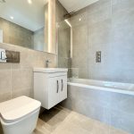 Modern bathroom with grey tiles and white fixtures.