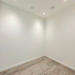 Empty white room with wooden floor and ceiling lights.