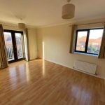Bright empty room with wooden flooring and windows.