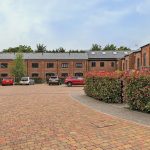 Brick buildings with parked cars and greenery.