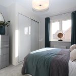 Modern bedroom with teal accents and large window.