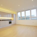 Modern kitchen with wooden floor and large windows.