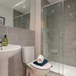 Modern bathroom with glass shower and grey tiles.