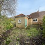 Back garden with brick outbuilding and bushes.
