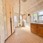 Old kitchen with wooden cabinets and tiled walls.