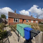 Red-brick bungalow with garden and bins outside.
