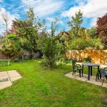Sunny garden with patio seating and lush greenery.