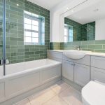 Modern bathroom with green tiles and white fixtures.