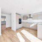 Modern kitchen with wooden flooring and white cabinets.