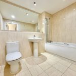Modern beige tiled bathroom with bath and toilet.