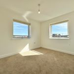 Bright empty room with two windows and beige carpet.