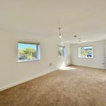 Spacious empty room with three windows and beige carpet.