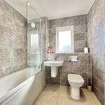 Modern grey tiled bathroom with bathtub and window.
