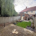 Suburban garden with decking, lawn, and brick house.