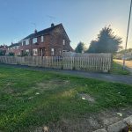 Suburban house with garden and fence at sunset.