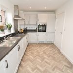 Modern white kitchen with herringbone floor and plants.