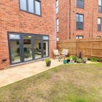 Modern patio with garden and brick building view.
