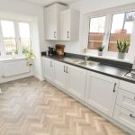 Modern kitchen with white cabinets and herringbone floor.