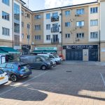 Shopping area with parked cars and various shops.