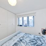 Modern bedroom with white wardrobes and large window.