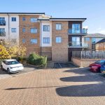 Modern apartment building with parked cars in foreground.