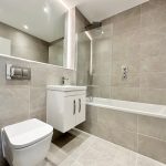 Modern grey-tiled bathroom with bathtub and vanity unit.