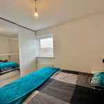 Modern bedroom with teal bedspread and mirror.