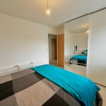 Modern bedroom with large mirrored wardrobe and teal bedding.