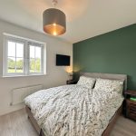 Cosy bedroom with green accent wall and window view.