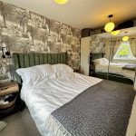Cosy bedroom with patterned wallpaper and mirrored wardrobe.