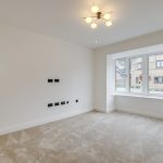Empty carpeted room with large window, chandelier above.