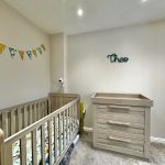 Neutral-toned nursery with cot, dresser, and bunting decor.