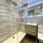 Modern bathroom with textured tiles and illuminated mirror.