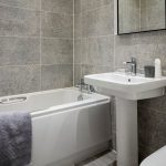 Modern bathroom with bathtub and grey tiles.