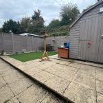 Backyard with shed, artificial grass, and bird feeder.