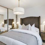 Modern bedroom with grey bed and mirrored wardrobe.