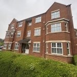 Red brick apartment building with green hedges.