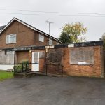 Boarded-up brick building with driveway in front.